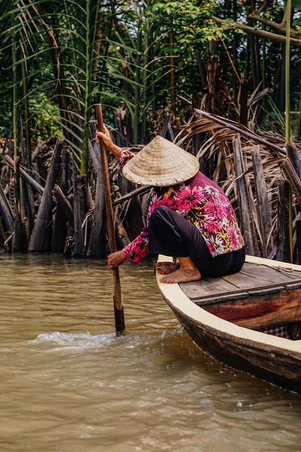 Người phụ nữ lớn tuổi đội nón lá chèo xuồng trên một kênh rạch ở đồng bằng sông Cửu Long